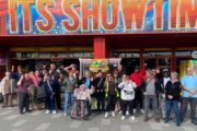 A large group of people standing outside a building with a banner saying 'It's Show Time'
