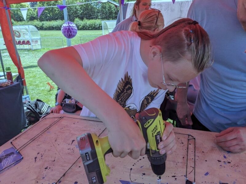 A young girl uses an electric drill to put a screw into a sheet of wood