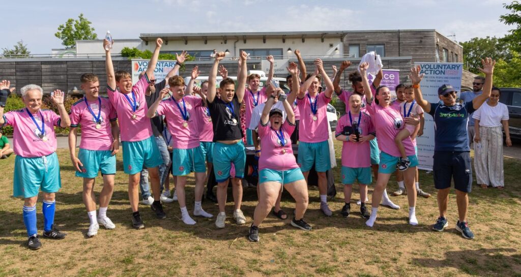 A football team in pink shirts and blue shorts waving their arms and cheering