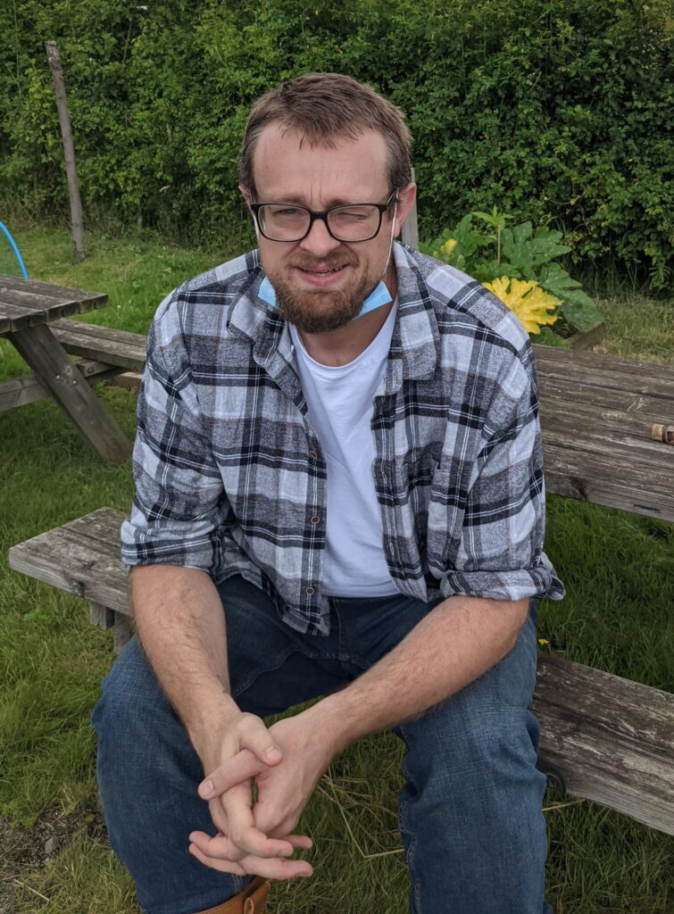 A man with glasses and a beard sitting on a picnic table bench